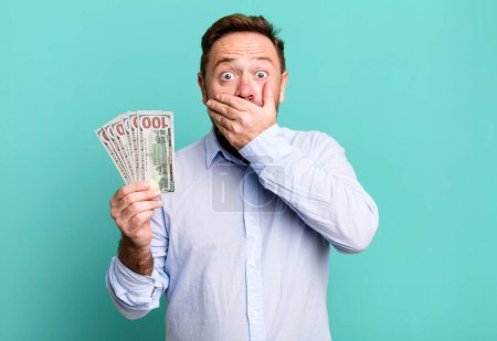 Téléchargez les photos : Middle age man covering mouth with hands with a shocked. dollar banknotes concept - en image libre de droit