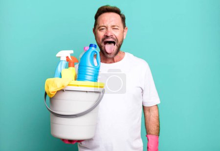 Photo for Middle age man with cheerful and rebellious attitude, joking and sticking tongue out. housekeeper with clean products - Royalty Free Image