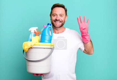 Foto de Hombre de mediana edad sonriendo y buscando amigable, mostrando el número cuatro. ama de llaves con productos limpios - Imagen libre de derechos