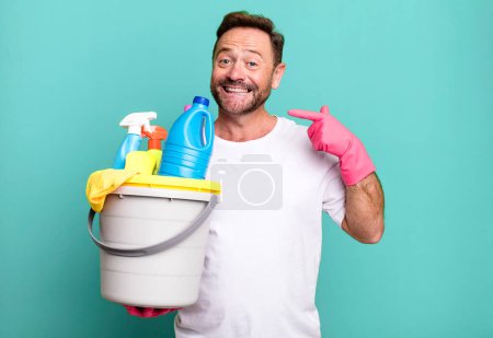 Foto de Hombre de mediana edad sonriendo con confianza apuntando a su propia sonrisa amplia. ama de llaves con productos limpios - Imagen libre de derechos
