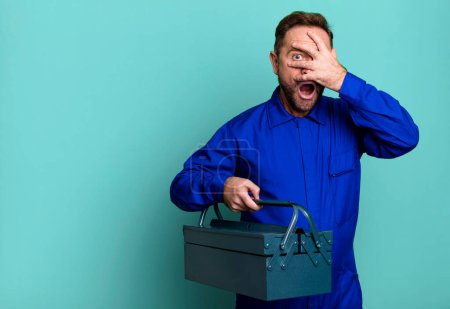 Photo for Middle age man looking shocked, scared or terrified, covering face with hand. plumber with a toolbox concept - Royalty Free Image