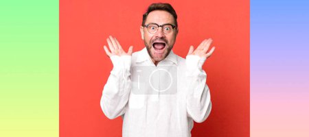 Photo for Looking happy and excited, shocked with an unexpected surprise with both hands open next to face - Royalty Free Image
