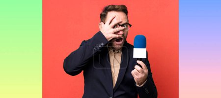 Foto de Hombre de mediana edad que parece sorprendido, asustado o aterrorizado, cubriendo la cara con la mano. periodista y un concepto de micrófono - Imagen libre de derechos