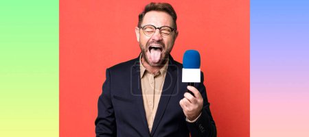 Foto de Hombre de mediana edad con actitud alegre y rebelde, bromeando y sacando la lengua. periodista y un concepto de micrófono - Imagen libre de derechos