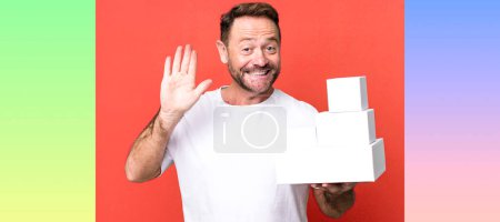 Photo for Middle age man smiling happily, waving hand, welcoming and greeting you. blank packages concept - Royalty Free Image