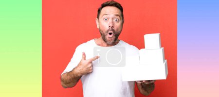 Foto de Hombre de mediana edad mirando sorprendido y sorprendido con la boca abierta, apuntando a sí mismo. concepto de paquetes en blanco - Imagen libre de derechos