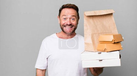 Photo for Middle age man looking happy and pleasantly surprised. delivery and fast food take away concept - Royalty Free Image
