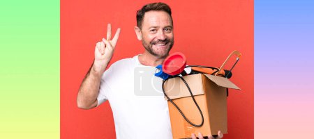 Téléchargez les photos : Homme d'âge moyen souriant et l'air amical, montrant numéro deux. bricoleur avec une boîte à outils - en image libre de droit
