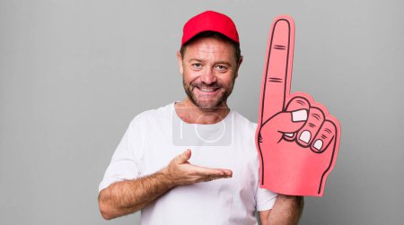 Téléchargez les photos : Homme d'âge moyen souriant joyeusement, se sentant heureux et montrant un concept. numéro un concept de ventilateur - en image libre de droit