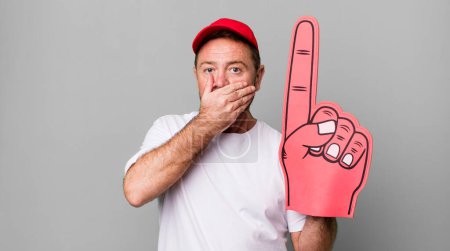 Téléchargez les photos : Homme d'âge moyen couvrant la bouche avec les mains avec un choc. numéro un concept de ventilateur - en image libre de droit