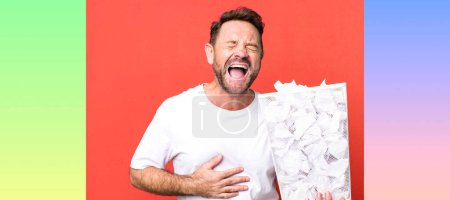 Photo for Middle age man laughing out loud at some hilarious joke. paper balls trash basket - Royalty Free Image