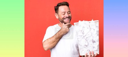 Photo for Middle age man smiling with a happy, confident expression with hand on chin. paper balls trash basket - Royalty Free Image