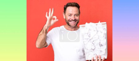 Foto de Hombre de mediana edad sintiéndose feliz, mostrando aprobación con gesto bien. bolas de papel papelera - Imagen libre de derechos