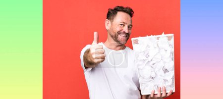 Photo for Middle age man feeling proud,smiling positively with thumbs up. paper balls trash basket - Royalty Free Image