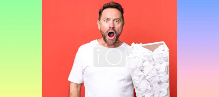 Photo for Middle age man looking very shocked or surprised. paper balls trash basket - Royalty Free Image