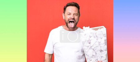 Foto de Hombre de mediana edad con actitud alegre y rebelde, bromeando y sacando la lengua. bolas de papel papelera - Imagen libre de derechos