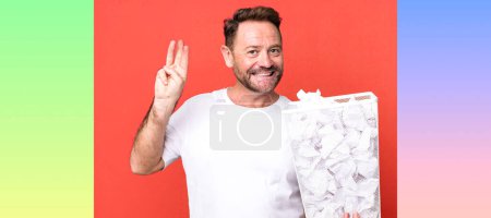Photo for Middle age man smiling and looking friendly, showing number three. paper balls trash basket - Royalty Free Image