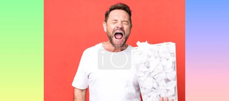 Photo for Middle age man shouting aggressively, looking very angry. paper balls trash basket - Royalty Free Image