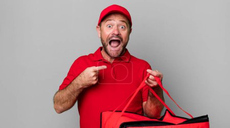 Foto de Hombre de mediana edad mirando emocionado y sorprendido señalando a un lado. repartidor de pizza - Imagen libre de derechos