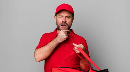 Photo for Middle age man with mouth and eyes wide open and hand on chin. pizza delivery man - Royalty Free Image