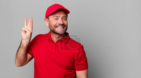 Foto de Hombre de mediana edad sonriendo y buscando amigable, mostrando el número tres. empleado de la empresa - Imagen libre de derechos