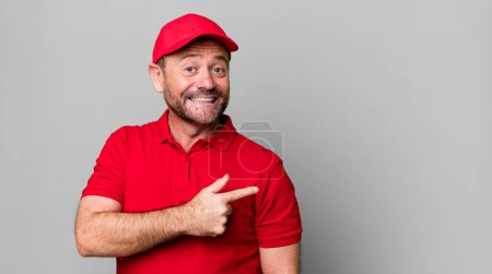 Foto de Hombre de mediana edad sonriendo alegremente, sintiéndose feliz y señalando hacia un lado. empleado de la empresa - Imagen libre de derechos