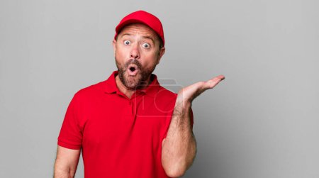 Photo for Middle age man looking surprised and shocked, with jaw dropped holding an object. company employee - Royalty Free Image