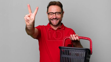 Photo for Middle age man smiling and looking happy, gesturing victory or peace. empty shopping basket concept - Royalty Free Image