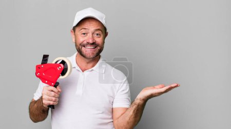 Téléchargez les photos : Homme d'âge moyen souriant joyeusement, se sentant heureux et montrant un concept. employé de l'entreprise - en image libre de droit