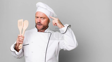 Foto de Hombre de mediana edad sintiéndose confundido y perplejo, mostrando que estás loco. concepto de chef y herramientas - Imagen libre de derechos