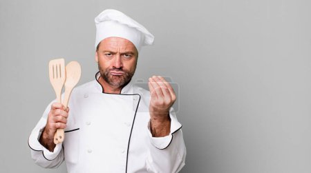 Foto de Hombre de mediana edad haciendo capice o gesto de dinero, diciéndote que pagues. concepto de chef y herramientas - Imagen libre de derechos