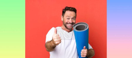 Photo for Middle age man feeling proud,smiling positively with thumbs up. with a yoga matt. fitness concept - Royalty Free Image