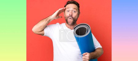Photo for Middle age man looking happy, astonished and surprised. with a yoga matt. fitness concept - Royalty Free Image