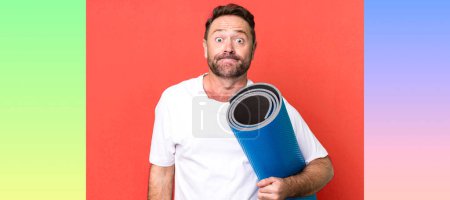 Photo for Middle age man shrugging, feeling confused and uncertain. with a yoga matt. fitness concept - Royalty Free Image