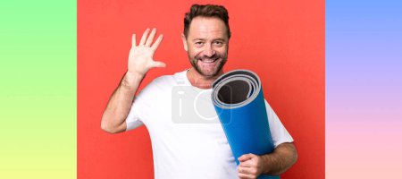 Foto de Hombre de mediana edad sonriendo y buscando amigable, mostrando el número cinco. con un mate de yoga. concepto de fitness - Imagen libre de derechos