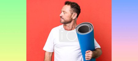Téléchargez les photos : Homme d'âge moyen sur la vue de profil penser, imaginer ou rêver. avec un tapis de yoga. concept de fitness - en image libre de droit