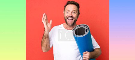 Photo for Middle age man feeling happy, surprised realizing a solution or idea. with a yoga matt. fitness concept - Royalty Free Image
