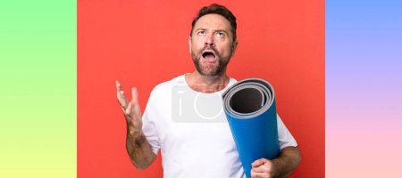 Téléchargez les photos : Homme d'âge moyen l'air désespéré, frustré et stressé. avec un tapis de yoga. concept de fitness - en image libre de droit