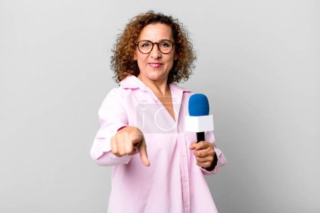 Photo for Pretty middle age woman pointing at camera choosing you. tv presenter with a microphone concept - Royalty Free Image