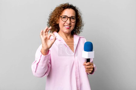 Photo for Pretty middle age woman feeling happy, showing approval with okay gesture. tv presenter with a microphone concept - Royalty Free Image