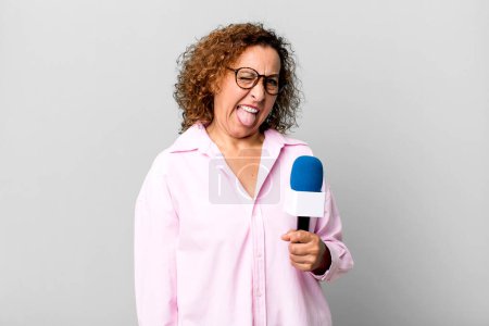 Foto de Bonita mujer de mediana edad con actitud alegre y rebelde, bromeando y sacando la lengua. presentador de televisión con un concepto de micrófono - Imagen libre de derechos