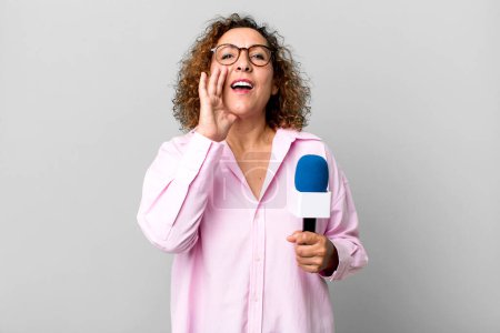Photo for Pretty middle age woman feeling happy,giving a big shout out with hands next to mouth. tv presenter with a microphone concept - Royalty Free Image