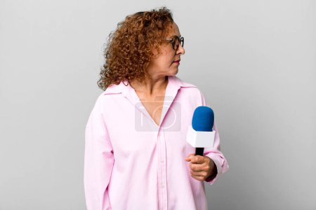 Foto de Mujer de mediana edad en vista de perfil pensando, imaginando o soñando despierto. presentador de televisión con un concepto de micrófono - Imagen libre de derechos