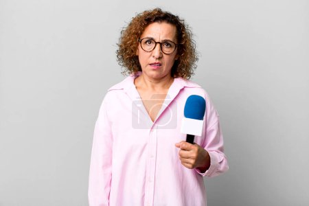 Foto de Mujer de mediana edad se siente desconcertado y confundido. presentador de televisión con un concepto de micrófono - Imagen libre de derechos