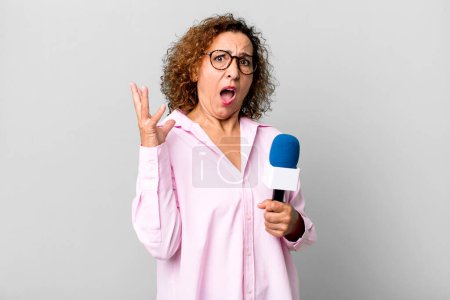 Photo for Pretty middle age woman screaming with hands up in the air. tv presenter with a microphone concept - Royalty Free Image
