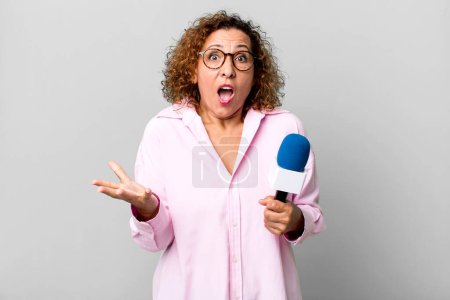 Foto de Mujer de mediana edad se siente muy sorprendido y sorprendido. presentador de televisión con un concepto de micrófono - Imagen libre de derechos