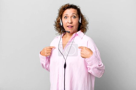 Foto de Mujer bastante mediana edad sentirse feliz y apuntando a sí mismo con un emocionado con un auricular. concepto de telemarketing - Imagen libre de derechos