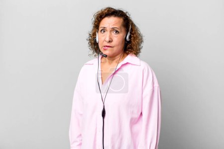 Foto de Mujer de mediana edad bastante buscando desconcertado y confundido con un auricular. concepto de telemarketing - Imagen libre de derechos