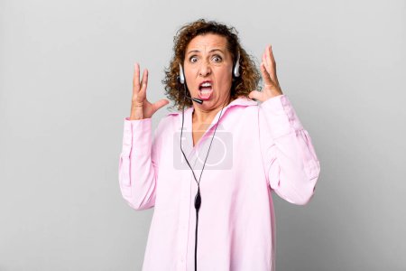 Foto de Mujer de mediana edad gritando con las manos en alto con un auricular. concepto de telemarketing - Imagen libre de derechos