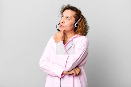 Foto de Mujer de mediana edad pensando, sintiéndose dudosa y confundida con un auricular. concepto de telemarketing - Imagen libre de derechos